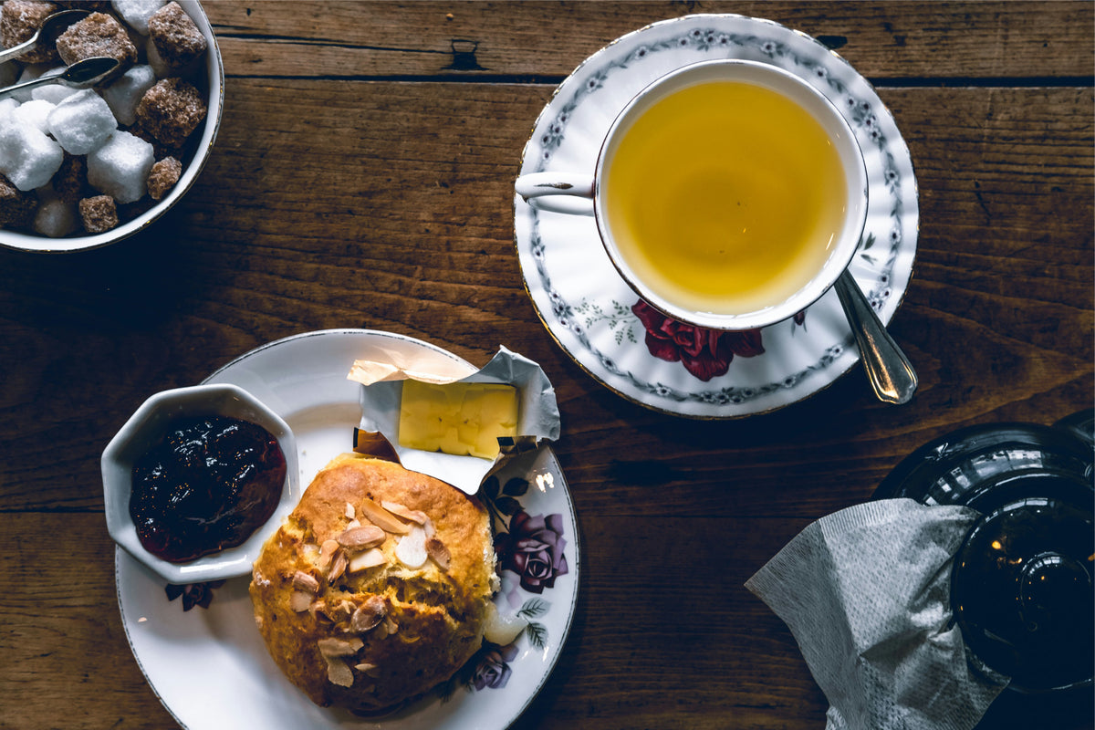 photo of decorative vintage tea cup, plates, and bowl full of sugar cubes.  Plate has scone and jam.