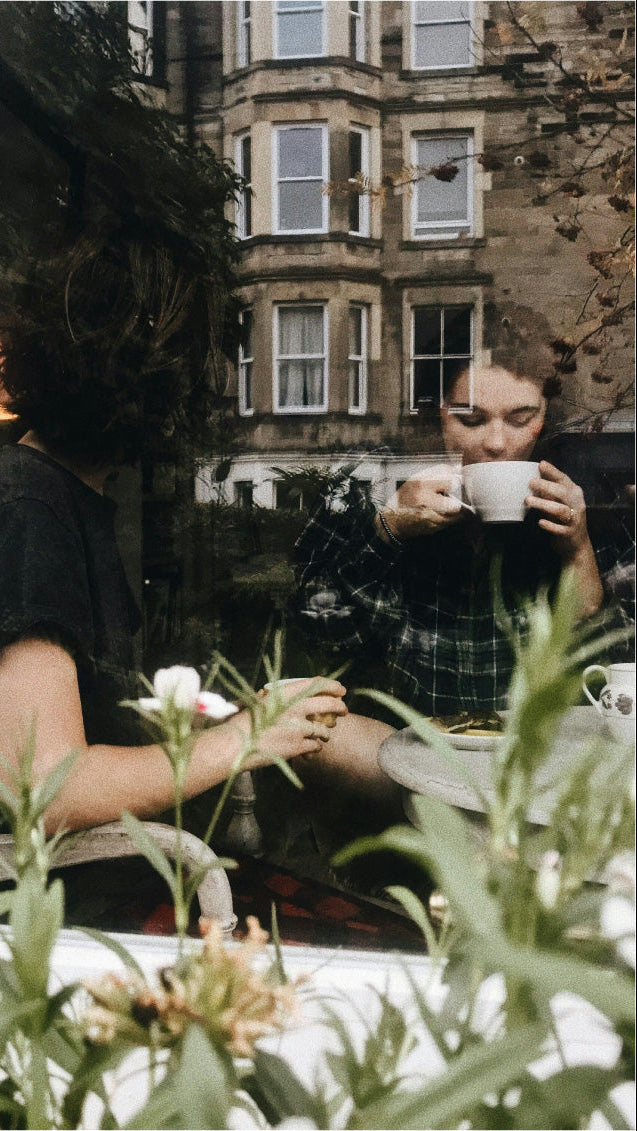 Artistic photo through a shop window of  two people drinking from teacups.  Reflection of the building across the street layered on top of image.