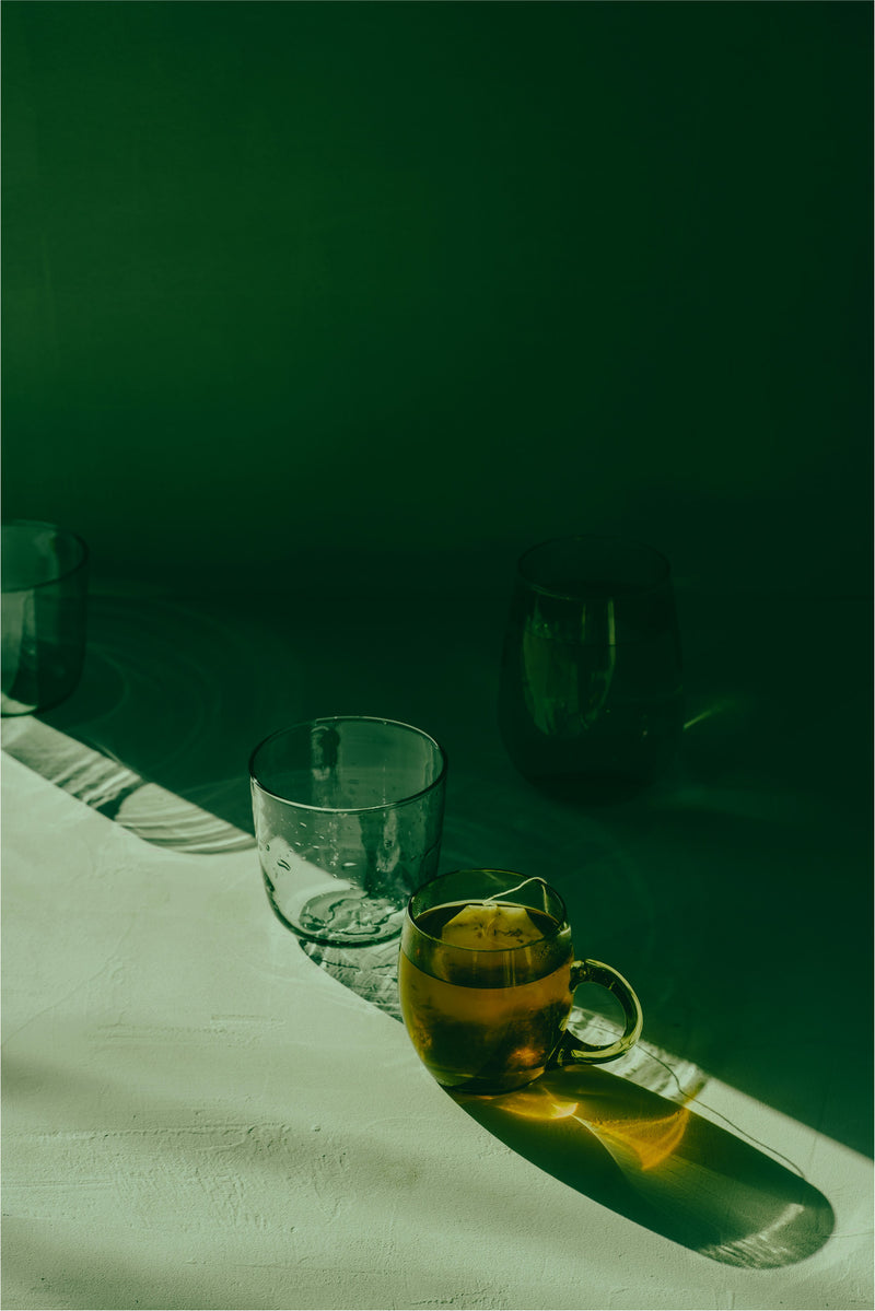 photo with green shadows, lighting shining in and clear glasses and a clear teacup full of tea