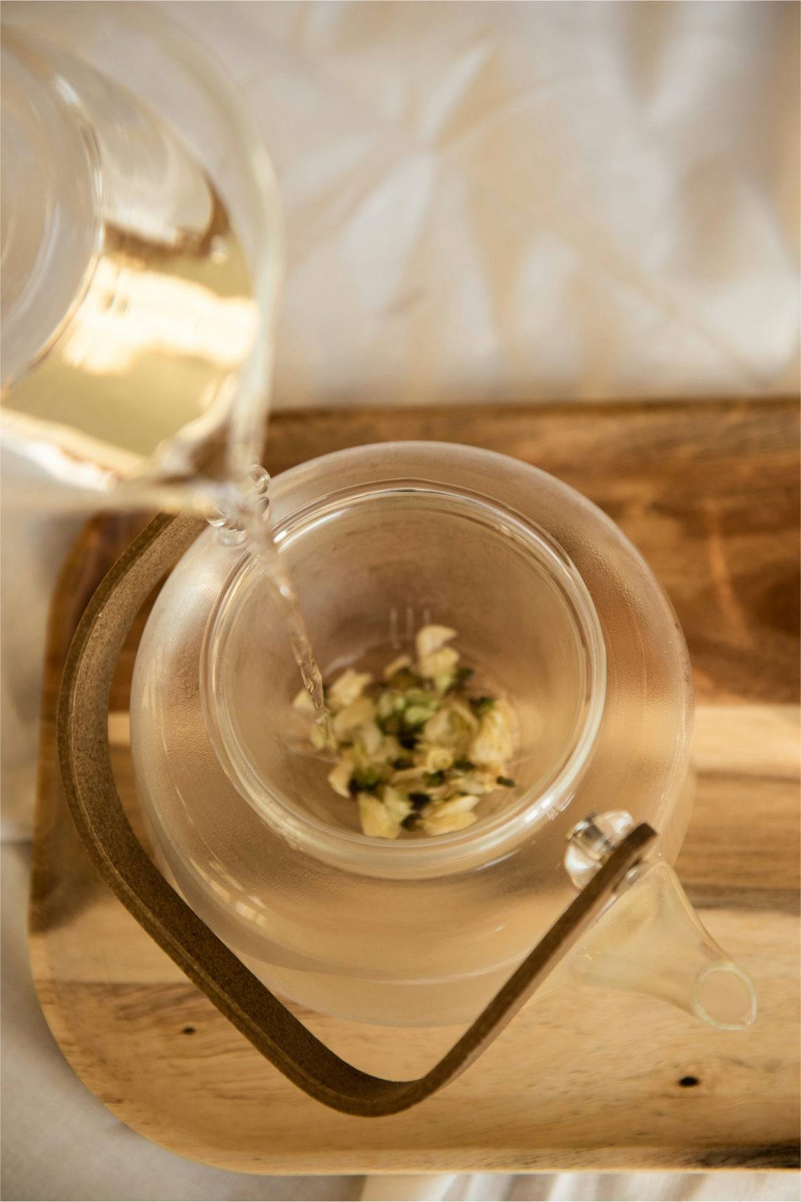 photo of clear tea pot with flower buds inside.  Warm lighting and a clear glass pouring water in to pot.