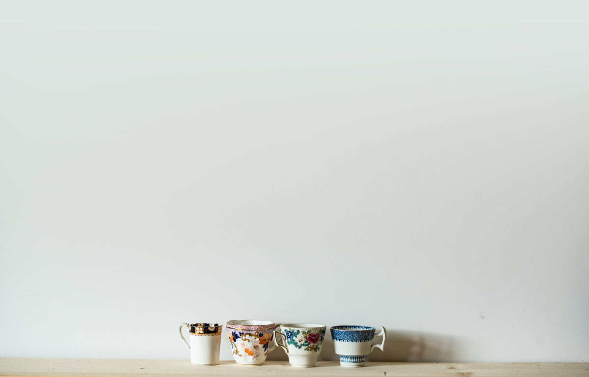 photo of 4 decorative vintage teacups against a white wall with lots of wall space in photo